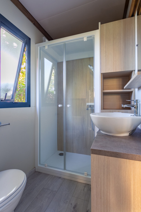 Baño moderno con cabina de ducha, ventana, inodoro y lavabo en Cottage Premium en Camping Paradis Le Giessen