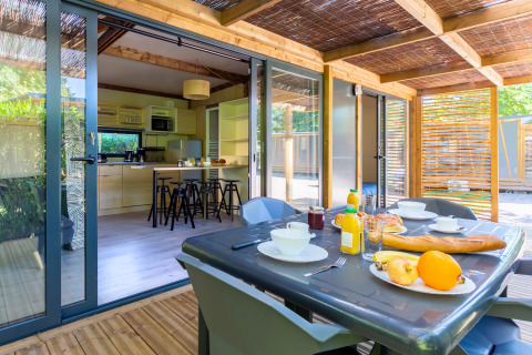 Mesa de desayuno en terraza cubierta con vista a la cocina de Cottage Premium en Camping Paradis Le Giessen, Francia.