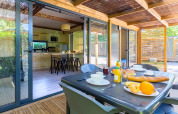 Mesa de desayuno en terraza cubierta con vista a la cocina de Cottage Premium en Camping Paradis Le Giessen, Francia.