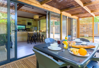 Mesa de desayuno en terraza cubierta con vista a la cocina de Cottage Premium en Camping Paradis Le Giessen, Francia.