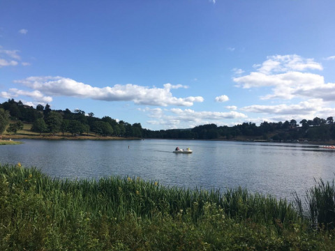 Peaceful lake view at Camping Paradis Les Chanterelles, Auvergne-Rhône-Alpes, France, with boat and greenery.