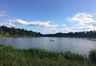 Rolig udsigt over en sø ved Camping Paradis Les Chanterelles i Auvergne-Rhône-Alpes med båd og grøn natur.