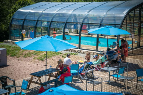 Piscine couverte de verre avec des vacanciers sous des parasols bleus au Camping Paradis Les Chanterelles, France.