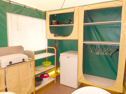 Interior de cocina de tienda con estufa, estanterías, armario y nevera en Camping Paradis Les Chanterelles, Francia.