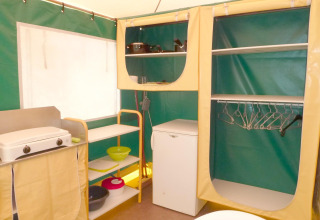 Intérieur cuisine sous tente avec réchaud, étagères et frigo au Camping Paradis Les Chanterelles, France.
