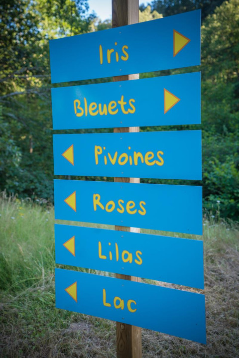 Blaues Wegweiser-Schild mit Blumen- und Seenamen im Camping Paradis Les Chanterelles in Frankreich.