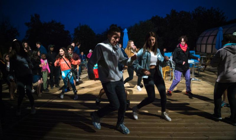 Gruppe unge danser udendørs om aftenen ved Camping Paradis Les Chanterelles i Auvergne-Rhône-Alpes, Frankrig.