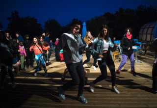 Gruppe unge danser udendørs om aftenen ved Camping Paradis Les Chanterelles i Auvergne-Rhône-Alpes, Frankrig.