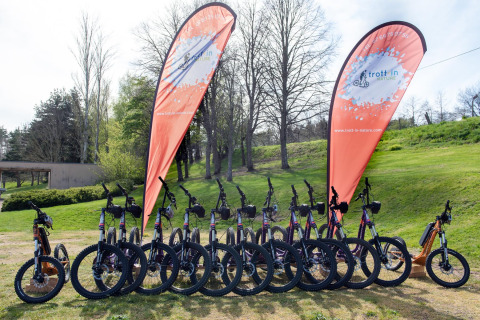 Fila de bicicletas eléctricas delante de dos banderas en Camping Paradis Les Chanterelles, Auvergne-Rhône-Alpes, Francia.