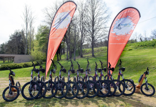 Fila de bicicletas eléctricas delante de dos banderas en Camping Paradis Les Chanterelles, Auvergne-Rhône-Alpes, Francia.