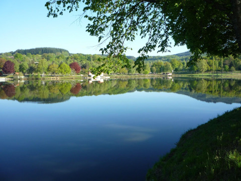 Peaceful lake near Saint-Rémy-sur-Durolle, Auvergne-Rhône-Alpes, France, with reflection of green trees on the water.