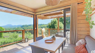 Interior de lodge moderno y luminoso con decoración de madera, comedor y terraza con vistas a colinas verdes.