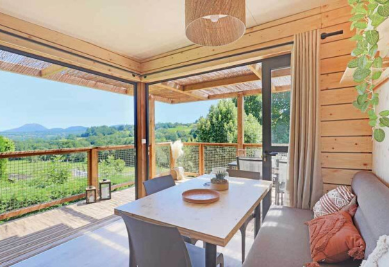 Interior de lodge moderno y luminoso con decoración de madera, comedor y terraza con vistas a colinas verdes.