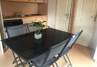 Zona pranzo con tavolo in vetro nero, quattro sedie e pianta in Chalet Eco presso Camping Paradis Les Chanterelles, Francia.
