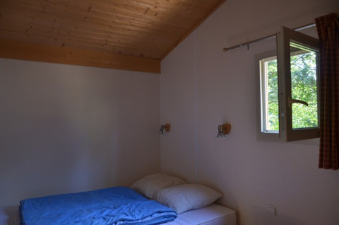 Une chambre simple au Chalet Eco MIVA au Camping Paradis Les Chanterelles en France avec une fenêtre ouverte.