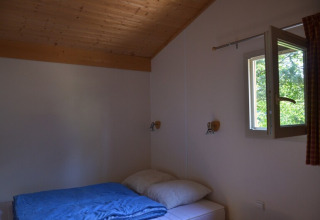 Une chambre simple au Chalet Eco MIVA au Camping Paradis Les Chanterelles en France avec une fenêtre ouverte.