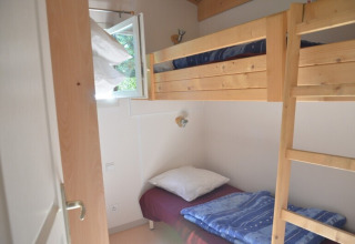 Petite chambre avec lits superposés en bois et fenêtre ouverte au Chalet Eco MIVA, Camping Paradis Les Chanterelles, France.