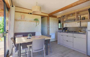 Interior luminoso de una cabaña con mesa de comedor, sillas, cocina y ventanales con vistas a la naturaleza.