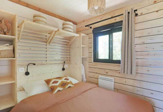 Lyst soveværelse på en lodge med træpaneler, enkeltseng, vindue, hylder og moderne indretning.