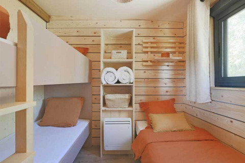 Knusse lodgekamer met lichte houten wanden, twee eenpersoonsbedden, planken en zonlicht door het raam.