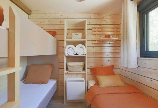 Acogedora habitación de lodge con paredes de madera clara, dos camas individuales y ventana soleada.