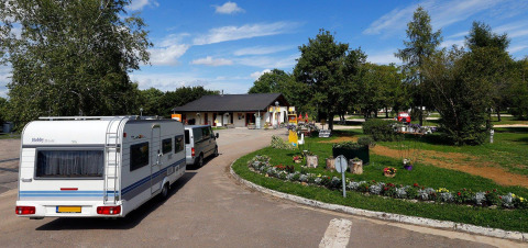 Campingvogn ankommer til Seasonova Camping Le Brabois i Grand Est, Frankrig, omgivet af grønne træer og blomster.