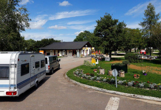 Caravana llegando a Seasonova Camping Le Brabois en Grand Est, Francia, rodeada de árboles y jardines con flores.