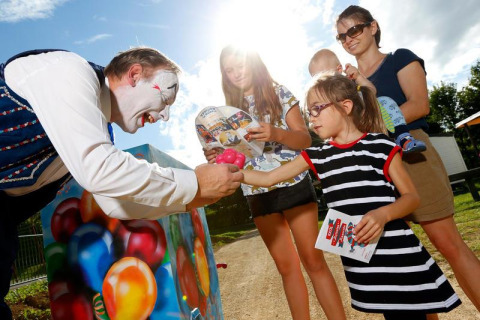 Ein Clown überreicht einem Kind einen Ballon, während eine Familie bei Sonnenschein in Grand Est, Frankreich zuschaut.