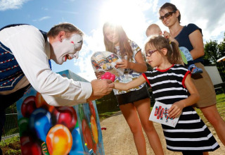 Ein Clown überreicht einem Kind einen Ballon, während eine Familie bei Sonnenschein in Grand Est, Frankreich zuschaut.