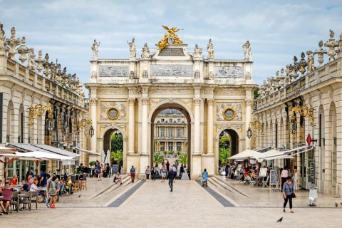 Foto eines eleganten Platzes mit Straßencafés und einem prächtigen Torbogen in Grand Est, Frankreich.