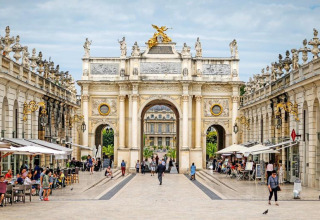 Foto de un arco monumental y una plaza animada con cafés al aire libre en Grand Est, Francia.