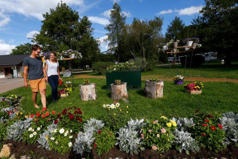 Pareja pasea junto a coloridos parterres de flores en Seasonova Camping Le Brabois, Grand Est, Francia.