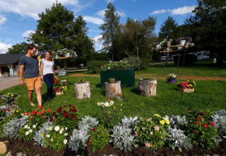 Pareja pasea junto a coloridos parterres de flores en Seasonova Camping Le Brabois, Grand Est, Francia.