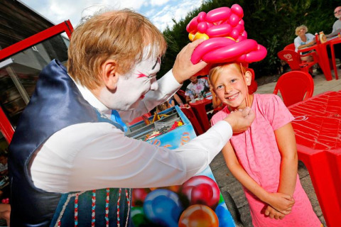 Un payaso hace un sombrero de globos para una niña sonriente en Seasonova Camping Le Brabois, Grand Est, Francia.
