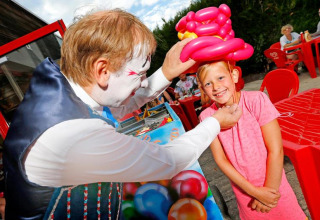 Un payaso hace un sombrero de globos para una niña sonriente en Seasonova Camping Le Brabois, Grand Est, Francia.