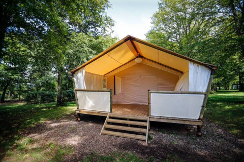 Tenda safari al Maasaï Lodge, immersa in una foresta verde, con veranda in legno rialzata all’ingresso.