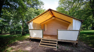 Tenda safari al Maasaï Lodge, immersa in una foresta verde, con veranda in legno rialzata all’ingresso.