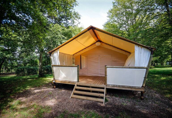 Tenda safari al Maasaï Lodge, immersa in una foresta verde, con veranda in legno rialzata all’ingresso.