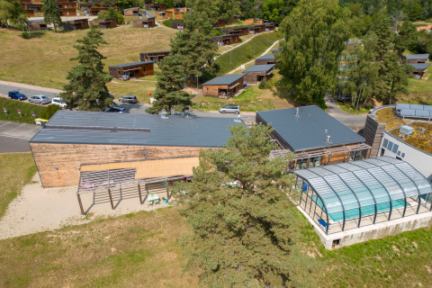 Vista aérea del parque vacacional Les Demeures du Lac en Francia, con cabañas, estacionamiento y piscina cubierta.
