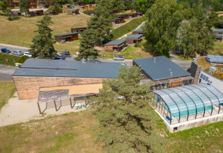 Luftaufnahme des Ferienparks Les Demeures du Lac mit Chalets, Parkplatz und überdachtem Pool in Frankreich.