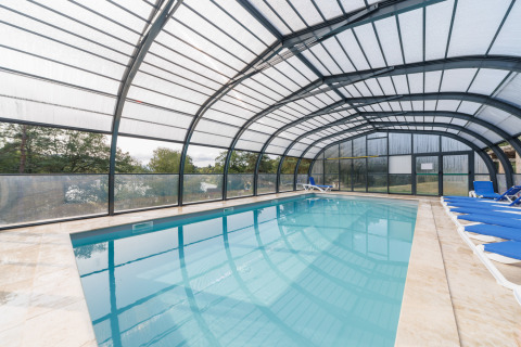 Piscina cubierta con tumbonas azules en Camping Holiday Park Les Demeures du Lac, Auvernia-Ródano-Alpes, Francia.