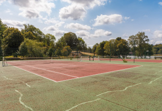 Außen-Tennisplatz im Ferienpark Les Demeures du Lac in Auvergne-Rhône-Alpes, Frankreich, mit Bäumen im Hintergrund.