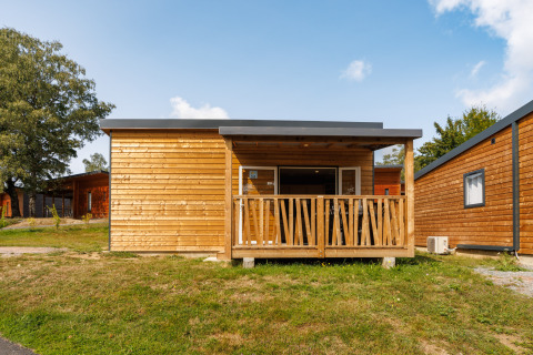 Houten lodge met overdekte veranda en grote ramen, gefotografeerd onder een deels bewolkte lucht.