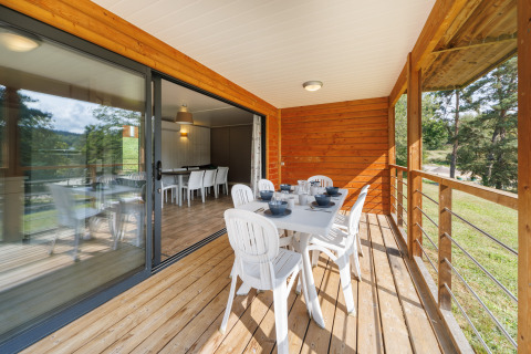 Terraza exterior de lodge de madera con mesa y sillas blancas preparadas para comer y vistas naturales.