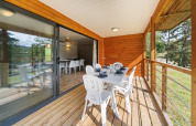 Terrasse einer Lodge mit Holzverkleidung, weißem Tisch und Stühlen, gedeckt zum Essen im Grünen.
