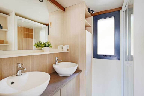 Baño moderno con dos lavabos blancos, espejo grande y paneles de madera en Premium cottage de Seasonova Camping Le Brabois.