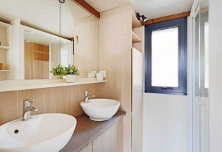 Baño moderno con dos lavabos blancos, espejo grande y paneles de madera en Premium cottage de Seasonova Camping Le Brabois.