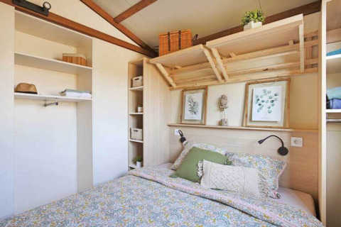 Dormitorio de una cabaña Premium en Seasonova Camping Le Brabois, Francia, con cama doble y estantes.