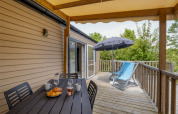 Houten terras met tafel, stoelen, ligstoelen en parasol bij Mobile home Comfort MIVA, Camping Le Plan d’Eau.
