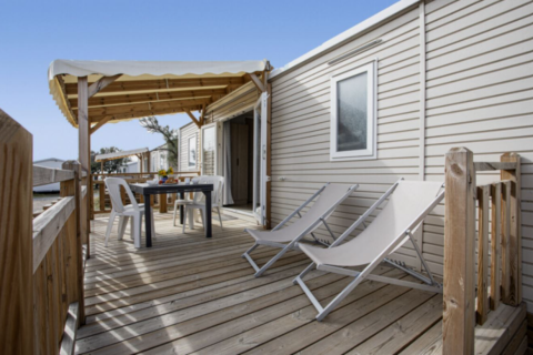 Houten terras aan Premium Mobile Home met loungestoelen, tafel, stoelen en houten overkapping.